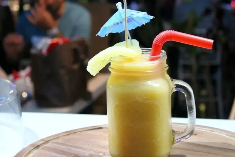 اسموتی زرد و تازه در لیوان جار، تزئین شده با میوه و چتر آبی کوچک. نوشیدنی خنک و تابستانی "رستوران ایتالیایی رو ب رو".
