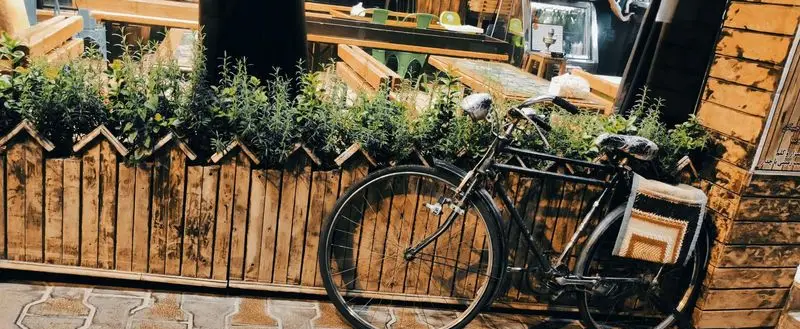 نمای زیبا از کافه دهه شصتی ها با دوچرخه قدیمی کنار گلدان چوبی پر از گیاهان سبز. فضایی دلنشین و نوستالژیک با دکوراسیون چوبی.