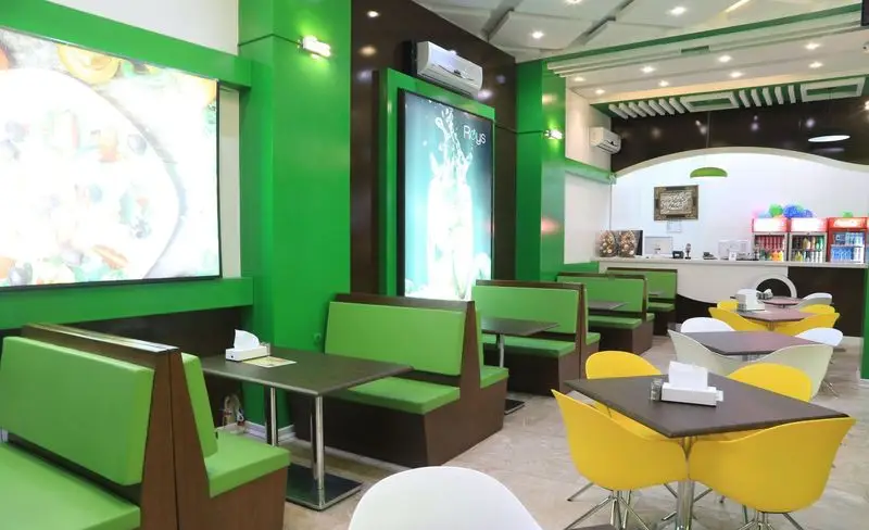 فضای داخلی مدرن و جذاب فست فود صدرا با میز و صندلی‌های راحت، دکوراسیون غالب سبز و قهوه‌ای، محیطی ایده‌آل برای صرف غذا.