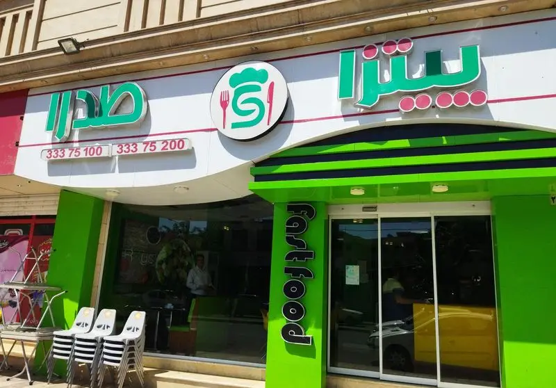 نمای کامل فست فود صدرا با تابلوهای سبز و سفید. نام صدرا و پیتزا، لوگوی شف و کارد و چنگال، و شماره تماس‌های ۳۳۳۷۵۱۰۰ و ۳۳۳۷۵۲۰۰.