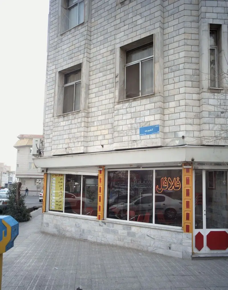 نمای بیرونی فست فود فلافل سید ۱۰۰۱ در خیابان آشوری، ساختمانی با نمای سنگی و تابلوی نئون فلافل، ارائه دهنده غذای محبوب فلافل.