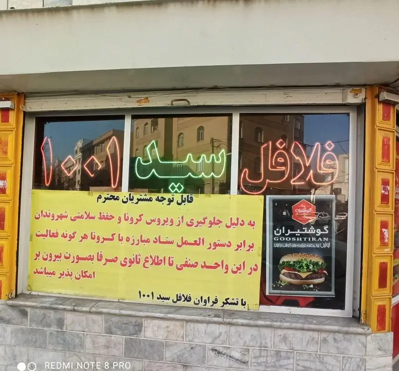فلافل سید ۱۰۰۱: نمای بیرونی این فست فود ایرانی با نئون‌های روشن و اطلاعیه مهم درباره سرویس بیرون‌بر در زمان کووید ۱۹.