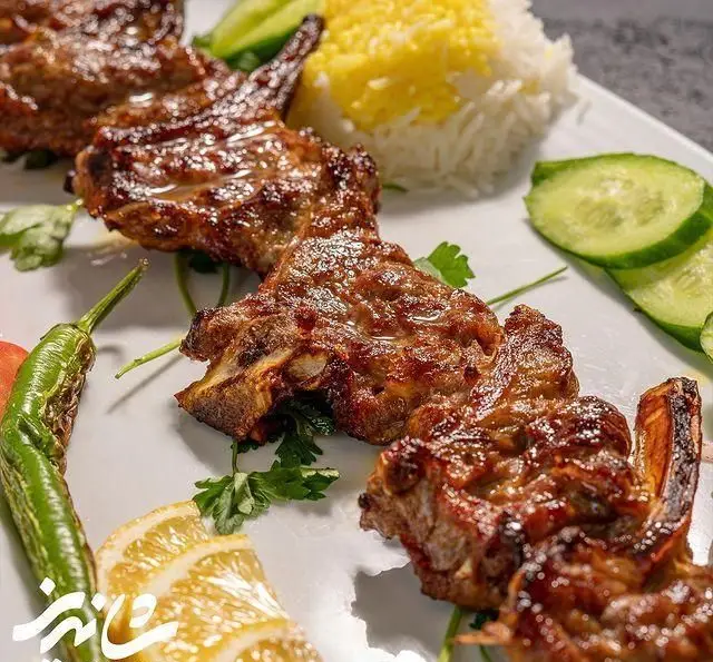 تصویری جذاب از شیشلیک یا دنده کباب مخصوص رستوران شاندیز، سرو شده با برنج قالبی و زعفرانی، خیار و فلفل سبز تند.