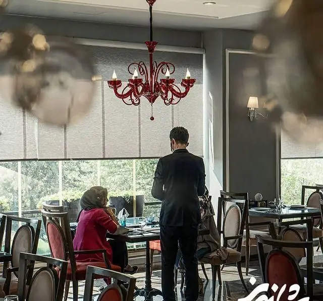 نمای داخلی رستوران شاندیز با لوستر قرمز رنگ خاص، چیدمان میز و صندلی‌های شیک، و مشتریان در فضایی آرام و دلپذیر.