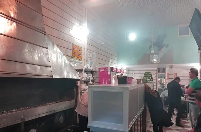 فضای داخلی شلوغ و پرجنب و جوش کبابی غدیر با کباب پز فعال و مشتریان در حال لذت بردن از کباب‌های تازه و خوشمزه.