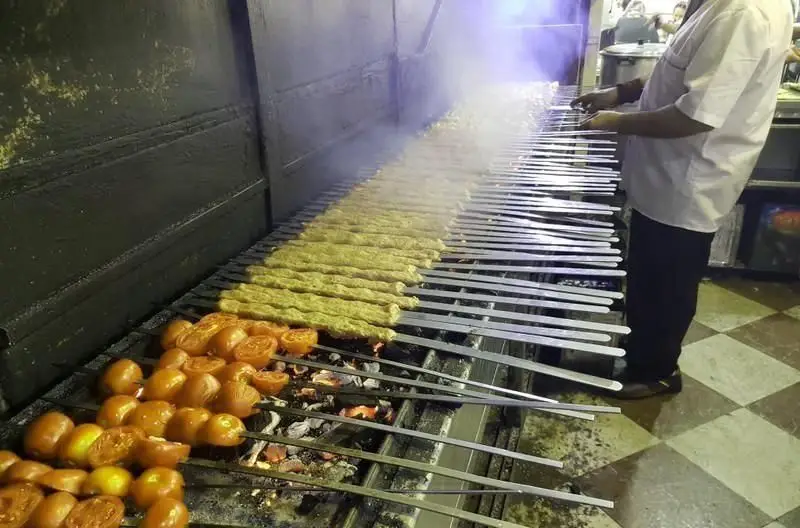 پخت کباب کوبیده و گوجه کبابی تازه روی منقل بزرگ در کبابی غدیر؛ آماده سازی بهترین کباب سنتی ایرانی برای مشتریان.