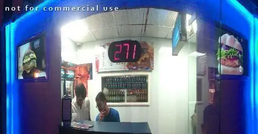 فضای داخلی خانه همبرگر با پرسنل مشغول، آماده‌سازی سفارشات و نمایشگر منوهای جذاب از همبرگرهای لذیذ و تازه.