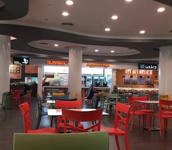 تصویری از فودکورت بزرگ و مدرن شامل رستوران فست فود منصوریان با صندلی‌های رنگارنگ و مشتریان در حال لذت بردن از غذا.