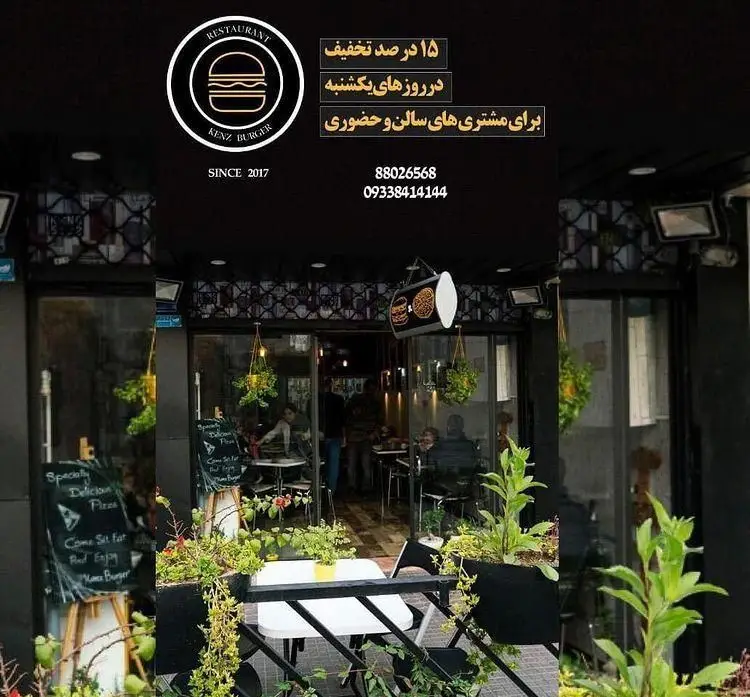 فست فود کنز برگر، نمای ورودی با فضای سبز و میزهای بیرونی. ۱۵ درصد تخفیف یکشنبه‌ها برای سفارش حضوری و سالن. شماره تماس.