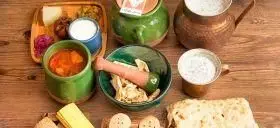 چیدمان زیبای غذای سنتی ایرانی با دیزی آبگوشت، نان داغ، لبنیات، ظروف سفالی و مسی در رستوران دیزی بار مزه بازار.