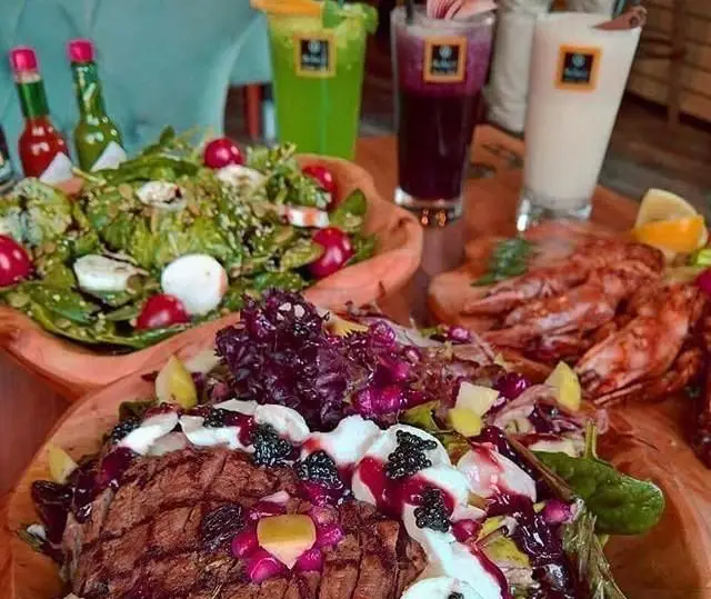 صحنه ای جذاب از میز پر از غذا و نوشیدنی‌های لذیذ کافی شاپ سولیس: سالاد سبز، استیک با سس بری، میگو گریل و سه نوع آبمیوه تازه.