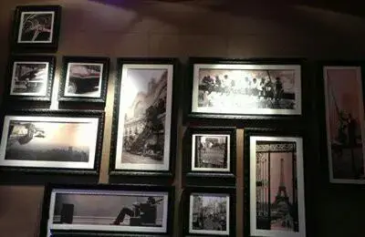 دیوار دکوراتیو رستوران ژینر با مجموعه ای از قاب عکس‌های هنری سیاه و سفید از مناظر شهری و صحنه‌های کلاسیک، فضایی دلنشین و خاص.