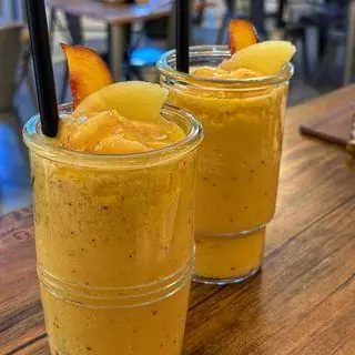 تصویری زیبا از دو لیوان اسموتی میوه‌ای و خنک هلو از بل کافه، با تزئین برش‌های هلو و نی، مناسب برای روزهای گرم تابستان.