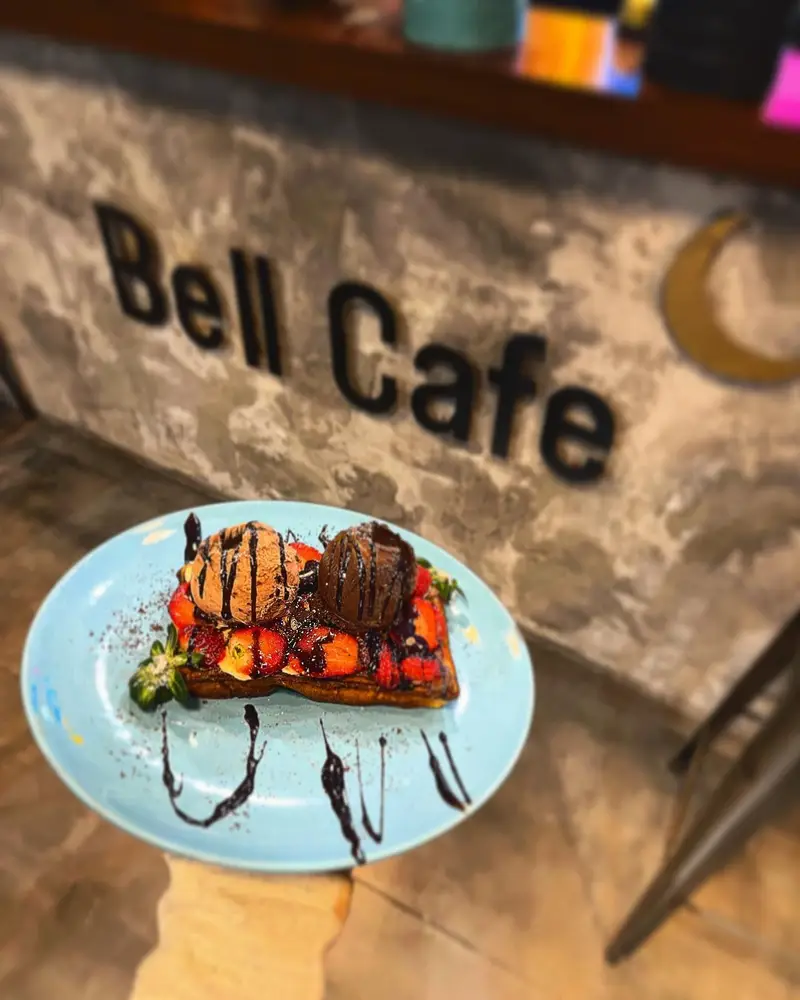تصویری از دسر بل کافه شامل تست فرانسوی با توت فرنگی، بستنی شکلاتی و سس غلیظ شکلات. بهترین شیرینی‌ها و نوشیدنی‌ها در محیط دلپذیر بل کافه.