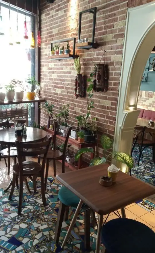 دکوراسیون داخلی رستوران جوان با دیوارهای آجری، گیاهان متنوع، پنجره بزرگ پرنور و میز و صندلی‌های چوبی در فضایی دنج و دلنشین.