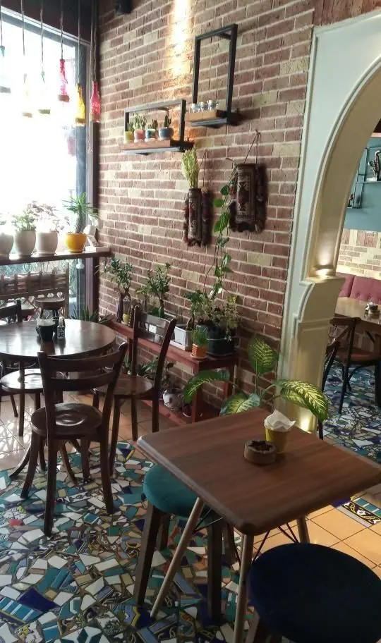 دکوراسیون داخلی رستوران و کافه جوان با دیوار آجری، گلدان‌های گیاه طبیعی، میزهای چوبی و کفپوش سنتی. فضایی دلپذیر برای مشتریان.