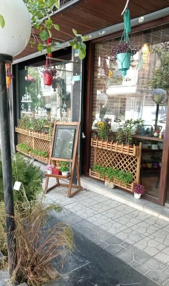 نمای ورودی رستوران جوان با دکوراسیون چوبی، گیاهان سرسبز، گلدان‌های آویز و تابلو منو جهت دعوت از مشتریان.