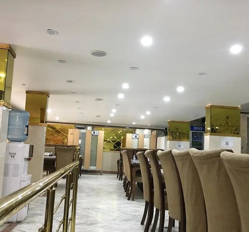 نمای داخلی رستوران جوان هنرور ۲ با میز و صندلی‌های مرتب، دکوراسیون طلایی و محیطی روشن و دلنشین، آماده پذیرایی از میهمانان.