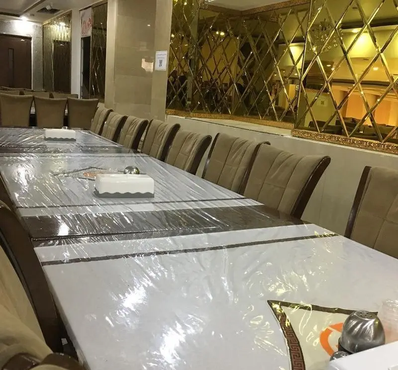 سالن غذاخوری بزرگ رستوران جوان هنرور ۲ با میزهای بلند آماده پذیرایی و صندلی‌های راحت، دیوارهای آینه‌ای و دکوراسیون شیک.