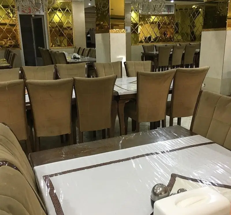 فضای داخلی رستوران جوان هنرور ۲ با میز و صندلی‌های قهوه‌ای رنگ، آینه‌های دکوراتیو طلایی و فضایی لوکس و شیک برای پذیرایی از مشتریان.
