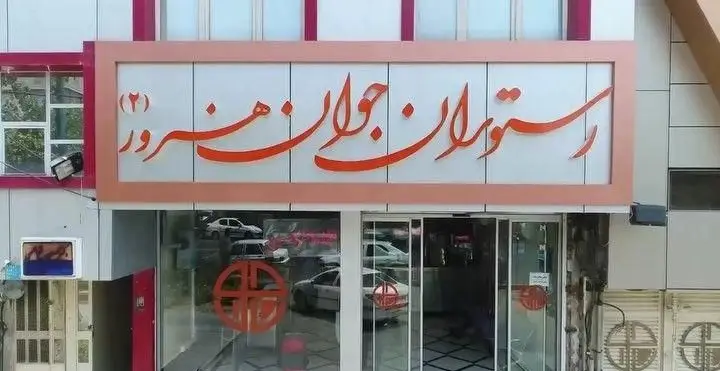 تصویری از نمای خارجی رستوران جوان هنرور ۲، تابلوی بزرگ و جذاب با خط فارسی و رنگ نارنجی، ورودی شیشه‌ای مجموعه