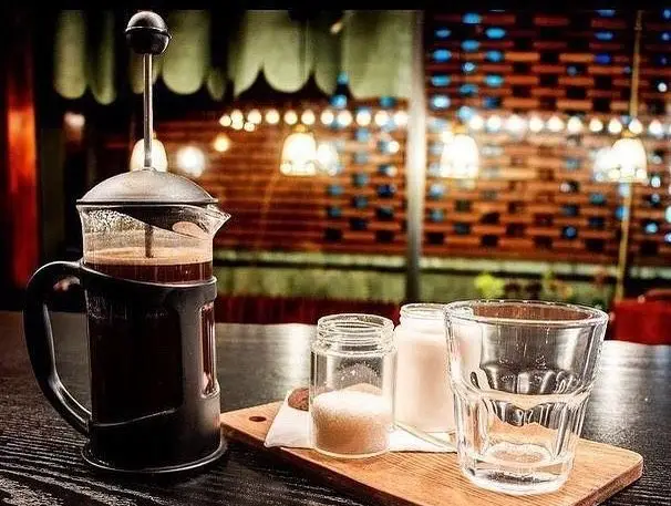 فرنچ پرس قهوه گرم و خوش‌طعم کافه مونو، آماده سرو با شکر و شیر در لیوانی تمیز. یک فضای دنج و دلپذیر برای تجربه نوشیدنی عالی.