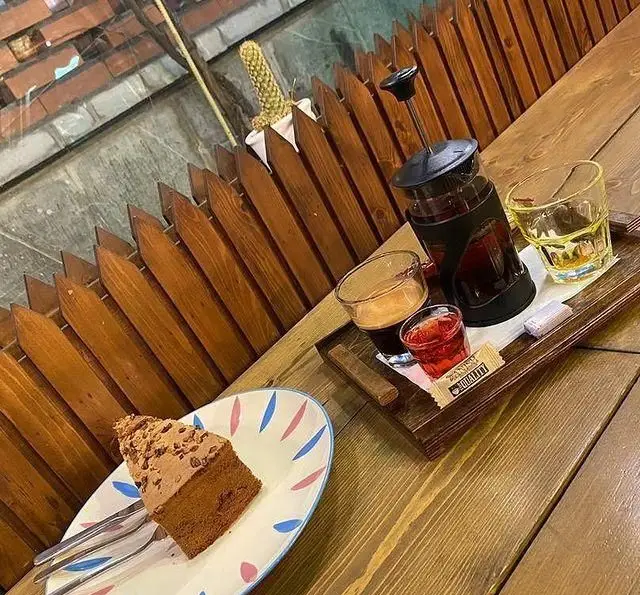 لذت دسر و قهوه در کافه مونو: کیک شکلاتی، اسپرسو، قهوه فرانسوی و نوشیدنی سرد روی میز چوبی با طراحی خاص.