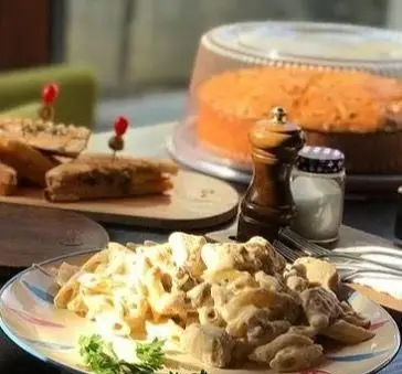 نمای نزدیک از میز پر از غذاهای لذیذ در کافه مونو. پاستا با سس سفید، ساندویچ‌های تست و کیک تازه در فضایی دلنشین و زیبا.