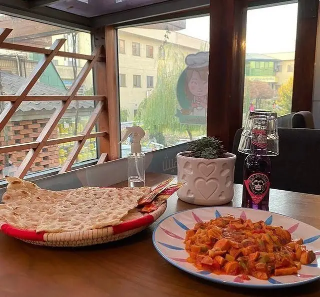 میزی با خوراک لذیذ، نان سنتی و نوشیدنی در کافه مونو با پنجره‌های مشرف به فضای سبز. تجربه‌ای دلنشین در کافه تهران.
