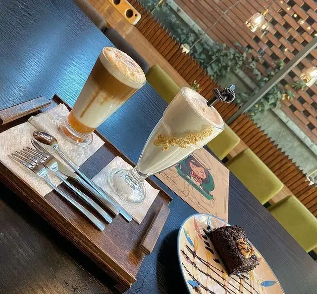 میز کافه مونو با نوشیدنی‌های خوشمزه، دسر براونی و قاشق و چنگال. فضایی دلنشین و دکوراسیون گرم و صمیمی. تجربه‌ای شیرین در کافه مونو.