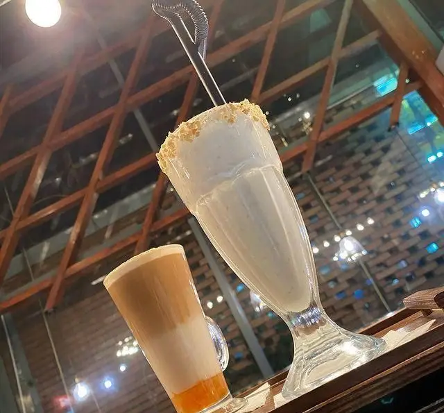 تجربه لذت‌بخش از نوشیدنی‌های خاص کافه مونو: میلک شیک خامه‌ای با تزئین کرانچی و یک لاته رنگی زیبا در فضای دلنشین و مدرن.