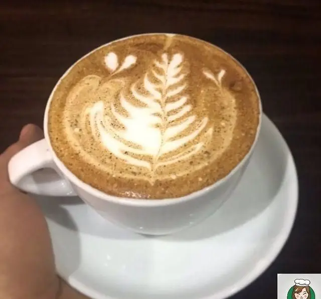 فنجانی قهوه لاته آرت با طرح زیبای برگ و جزئیات هنرمندانه روی فوم، نشان‌دهنده مهارت باریستا و تجربه بی‌نظیر در کافه مونو است.