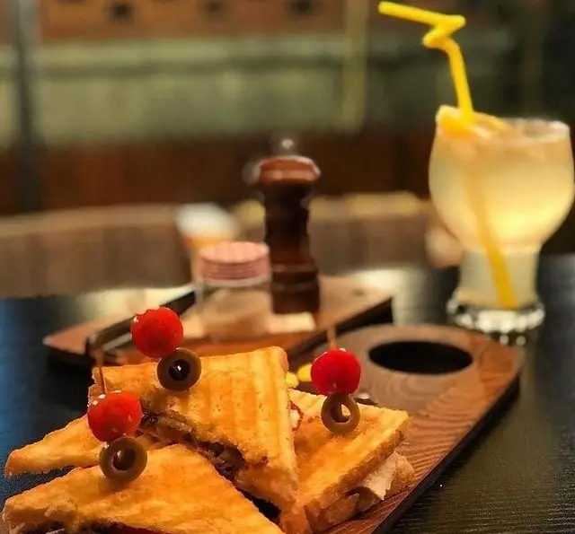 ساندویچ‌های گریل‌شده خوشمزه با تزئین زیتون و گیلاس، همراه با یک نوشیدنی خنک در کافه مونو، انتخابی عالی از منوی متنوع