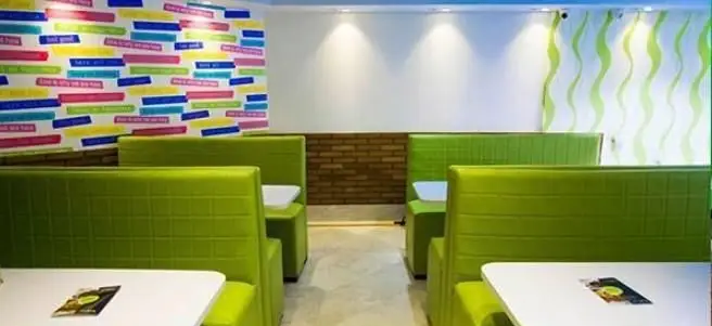 فضای داخلی فست فود پانچیک با صندلی‌های لیمویی رنگ، میزهای سفید، دیوارهای طرح‌دار جذاب و نورپردازی مدرن. محیطی شیک و دلنشین.