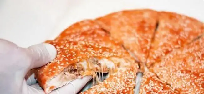 برش نان ساندویچ مغزدار ویژه فست فود پانچیک با پنیر آب شده و کنجد فراوان که توسط دست با دستکش سفید گرفته شده.