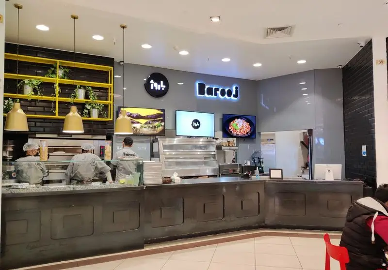 نمای داخلی رستوران فست فود باروژ با آشپزهای در حال پخت غذا، پیشخوان مدرن و نمایشگرهای منوی جذاب. محیطی دلنشین برای مشتریان.