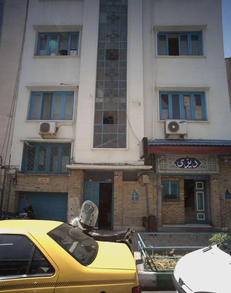 نمای بیرونی رستوران دیزی سرا با تابلوی کاشی‌کاری آبی، ورودی آجری و پنجره‌های آبی، در یک خیابان شلوغ با ماشین‌های پارک شده.