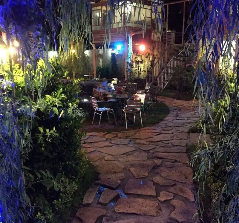 فضای باز رستوران گل یخ در شب، با مسیر سنگی، میز و صندلی‌های چیده شده، نورپردازی جذاب و محیط سرسبز و دلنشین.