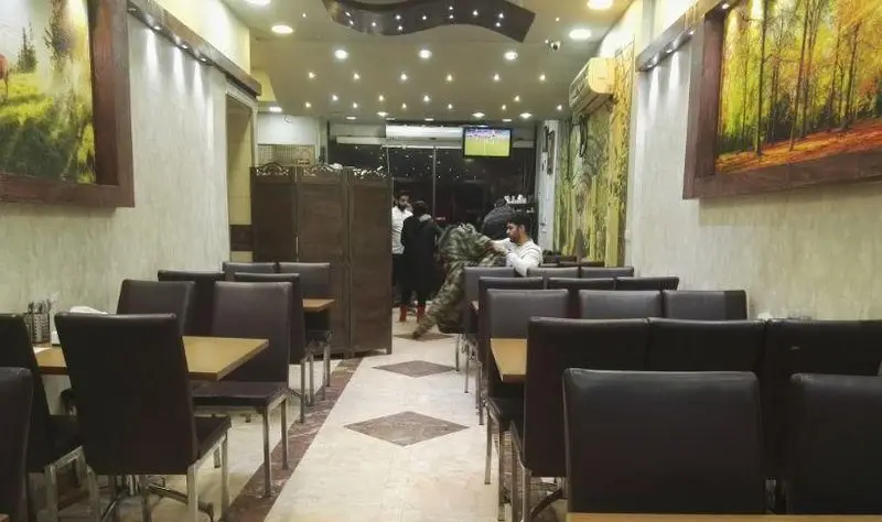 تصویری از فضای داخلی رستوران گل یخ: میز و صندلی‌های شیک، دکوراسیون با نقاشی‌های طبیعت و تلویزیون، محیطی آرام و دلنشین برای مشتریان.