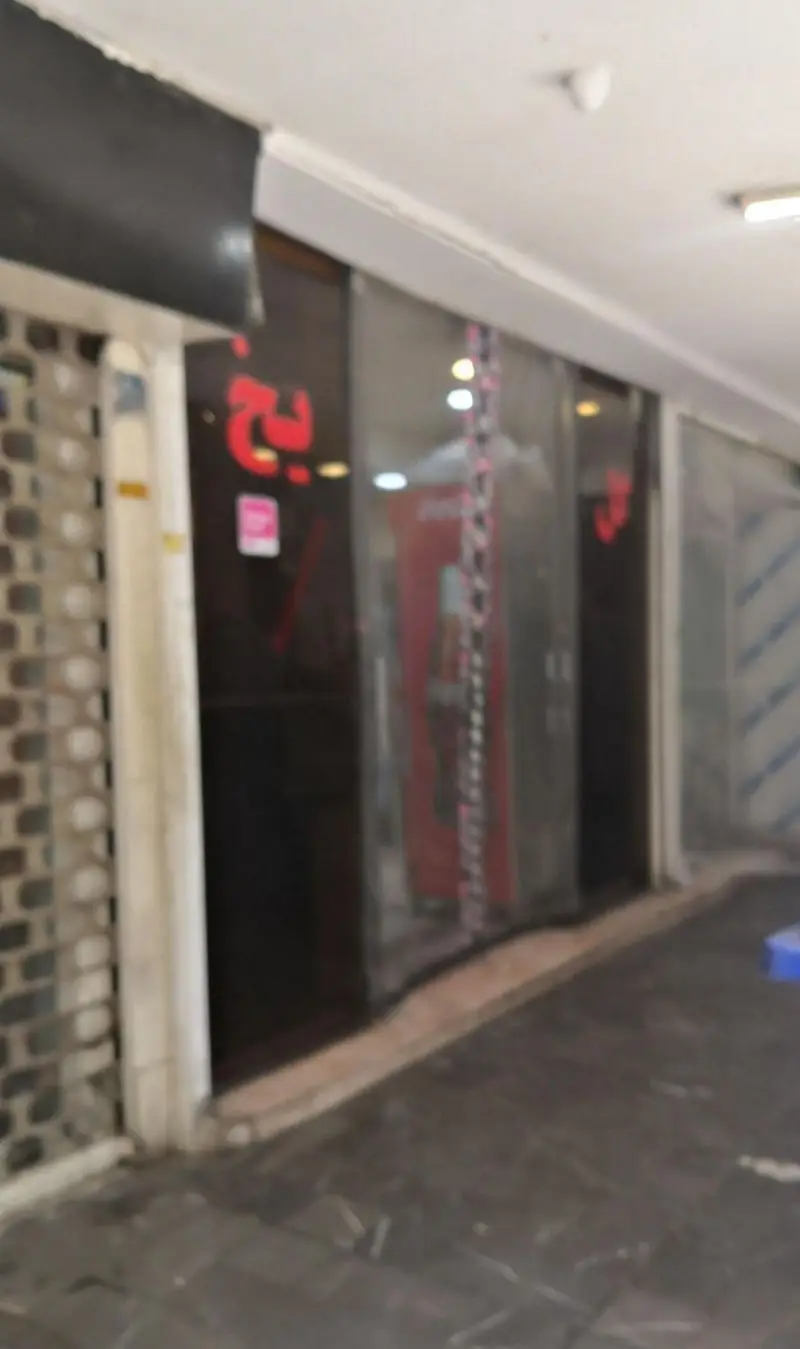 تصویری از نمای بیرونی رستوران گل یخ در یک مجتمع تجاری با ویترین شیشه ای بزرگ، ورودی با کرکره فلزی و تابلوی نئونی قرمز.