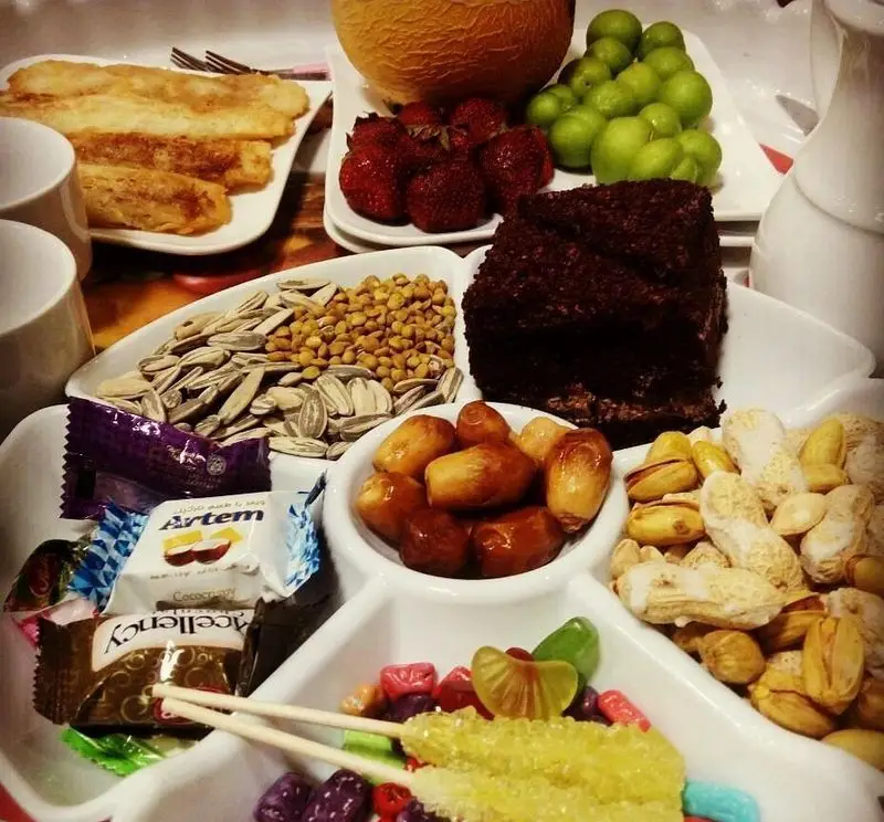 سینی پذیرایی ویژه و مفصل رستوران گل یخ: خرما، انواع آجیل، کیک شکلاتی، میوه‌های تازه و شیرینی‌های رنگارنگ.