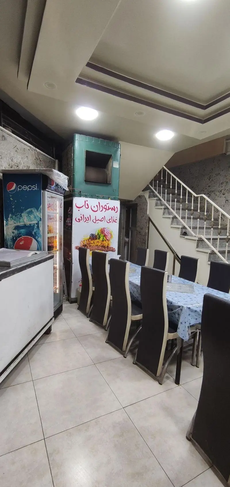 فضای داخلی رستوران ناب با میز و صندلی‌های شیک، یخچال پپسی و تابلوی غذای اصیل ایرانی. محیطی تمیز و مناسب برای تجربه کباب.