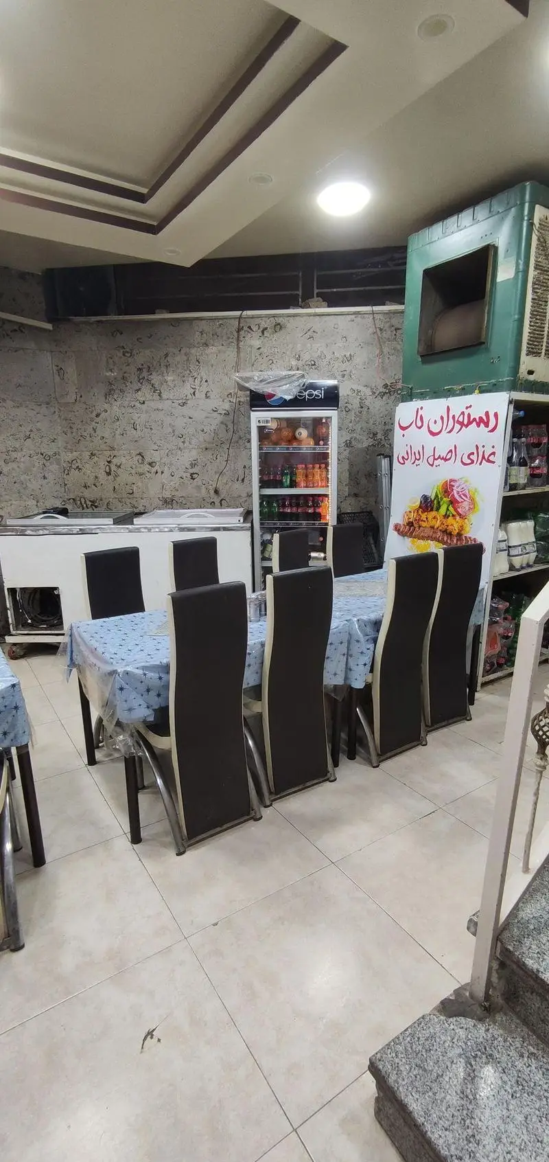 دکوراسیون داخلی رستوران ناب، با میز و صندلی‌های شیک، یخچال نوشیدنی پپسی و منوی جذاب غذای اصیل ایرانی.