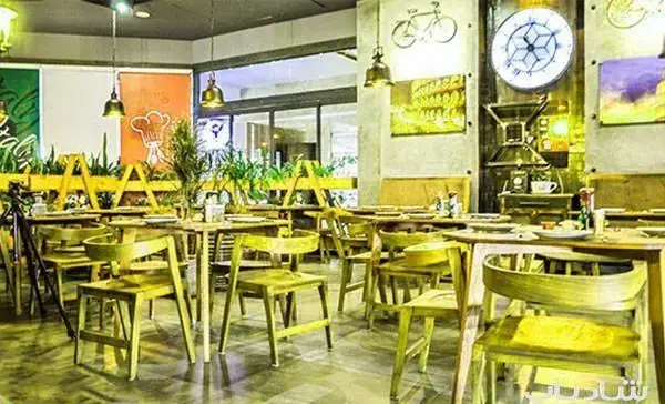 فضای داخلی دنج و دلنشین رستوران ایتالیایی اسپرلوس با چیدمان میز و صندلی‌های چوبی لیمویی، دکوراسیون خاص ایتالیایی و گیاهان.