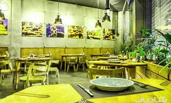 فضای داخلی شیک و مدرن رستوران ایتالیایی اسپرلوس با میز و صندلی‌های چوبی، دکوراسیون هنری و گیاهان سبز برای تجربه غذایی دلپذیر.