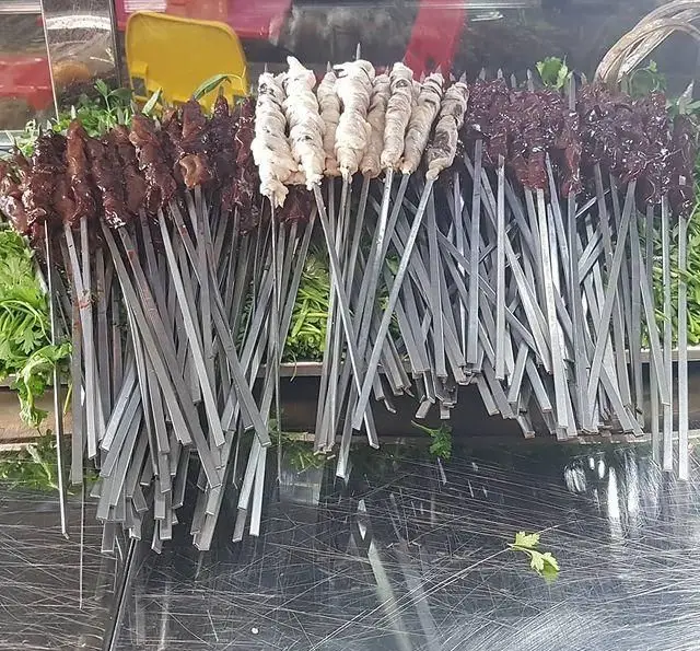 کباب‌های جگر تازه، دل و قلوه روی سیخ‌های فلزی در جگرسرای لیموترش. آماده برای پخت، همراه با سبزیجات معطر.