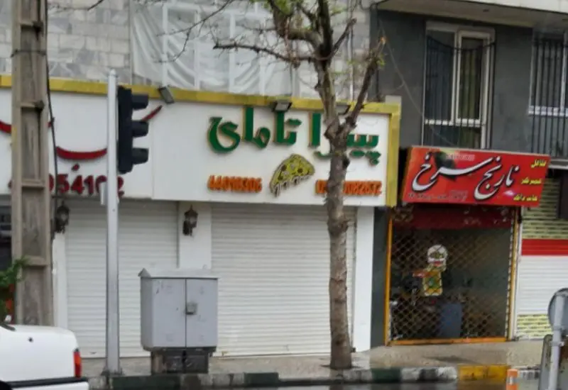 نمای بیرونی رستوران فست فود پیتزا تامای با تابلوی سبز رنگ روشن، شامل نام، نماد پیتزا و شماره تماس روی تابلو.