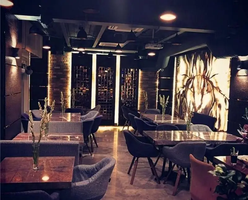 دکوراسیون داخلی لوکس کافه فرسکو با میزهای چوبی، صندلی‌های راحتی خاکستری، دیوارهای آجری و نورپردازی هنری، فضایی مدرن و دنج.