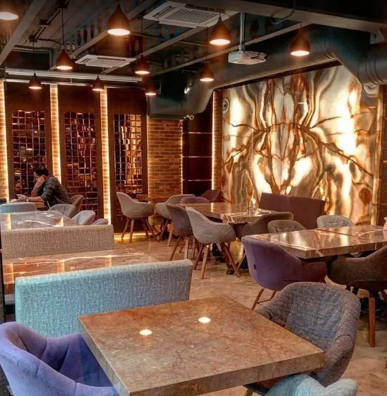 دکوراسیون داخلی کافه فرسکو: محیطی مدرن و دنج با نورپردازی گرم، میز و صندلی‌های شیک و راحت، و دیوار سنگی نورانی خیره‌کننده.