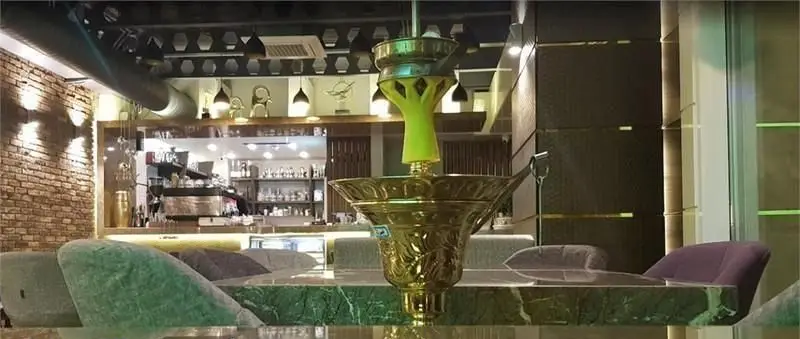 نمای داخلی کافه فرسکو: قلیان طلایی، میز مرمری سبز، صندلی‌های راحت، بار قهوه با دستگاه اسپرسو و دکوراسیون شیک و مدرن.